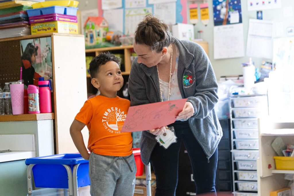 Image of an adult talking to a child about their project.