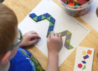 A young boy matching colored tiles to a papaer that has tiles printed in a design.