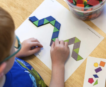 A young boy matching colored tiles to a papaer that has tiles printed in a design.