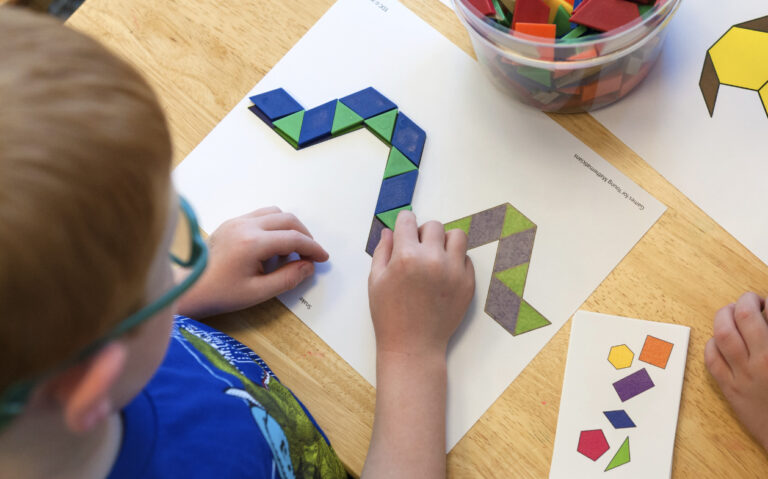 A young boy matching colored tiles to a papaer that has tiles printed in a design.