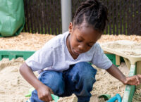 Little Black girl playing in a sandbox.