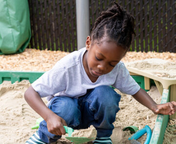 Little Black girl playing in a sandbox.